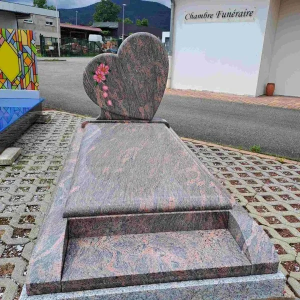 Monument funéraire en granit veiné avec stèle en forme de cœur gravée de fleurs