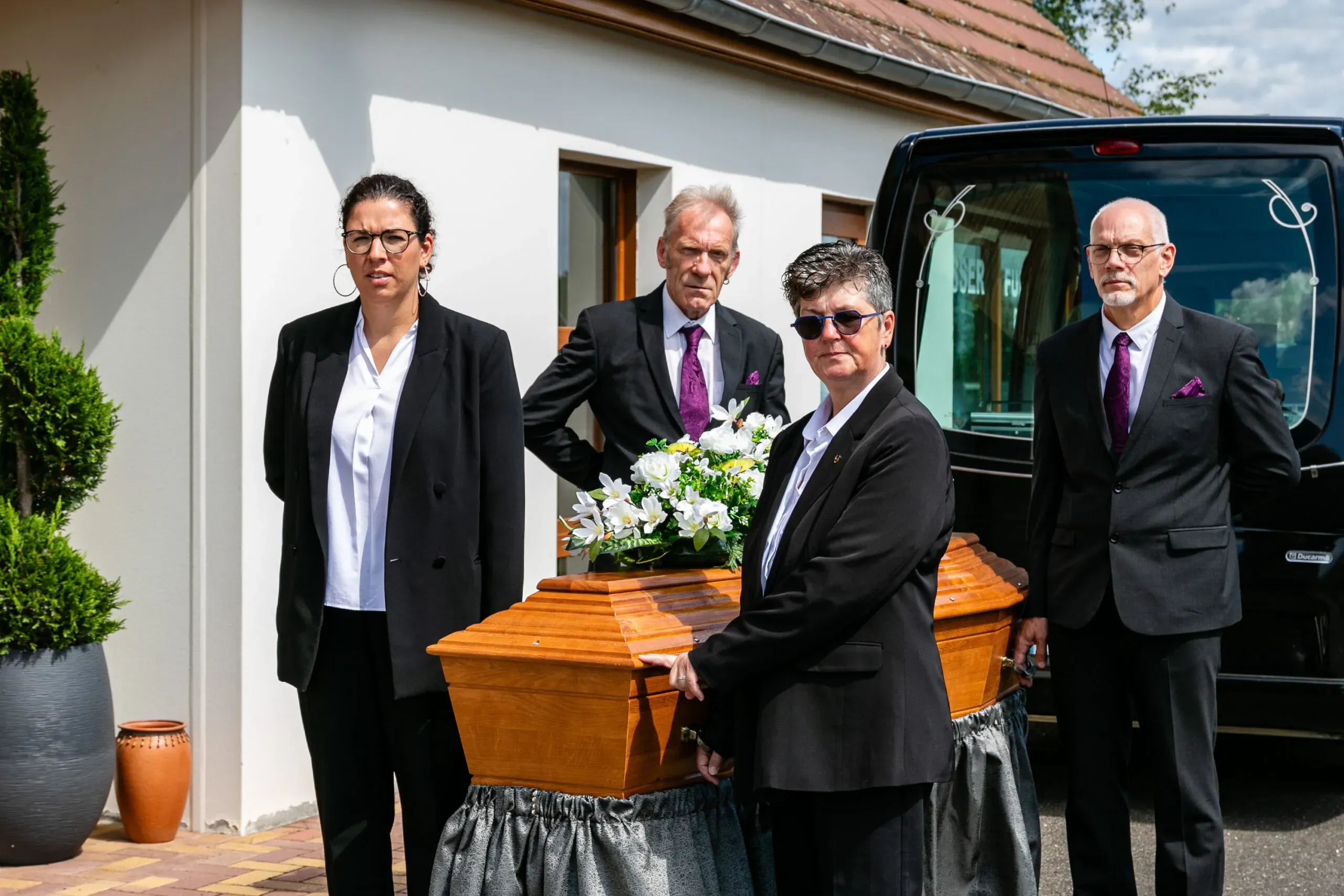 Quatre porteurs funéraires en tenue professionnelle entourant un cercueil en bois